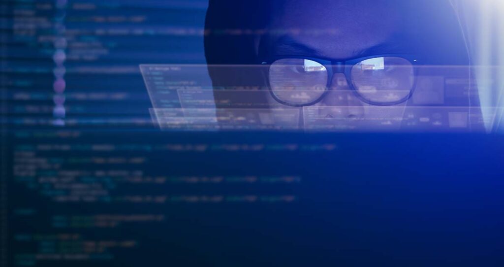 A imagem mostra o reflexo de um homem de óculos na tela de um computador com diversos códigos.
