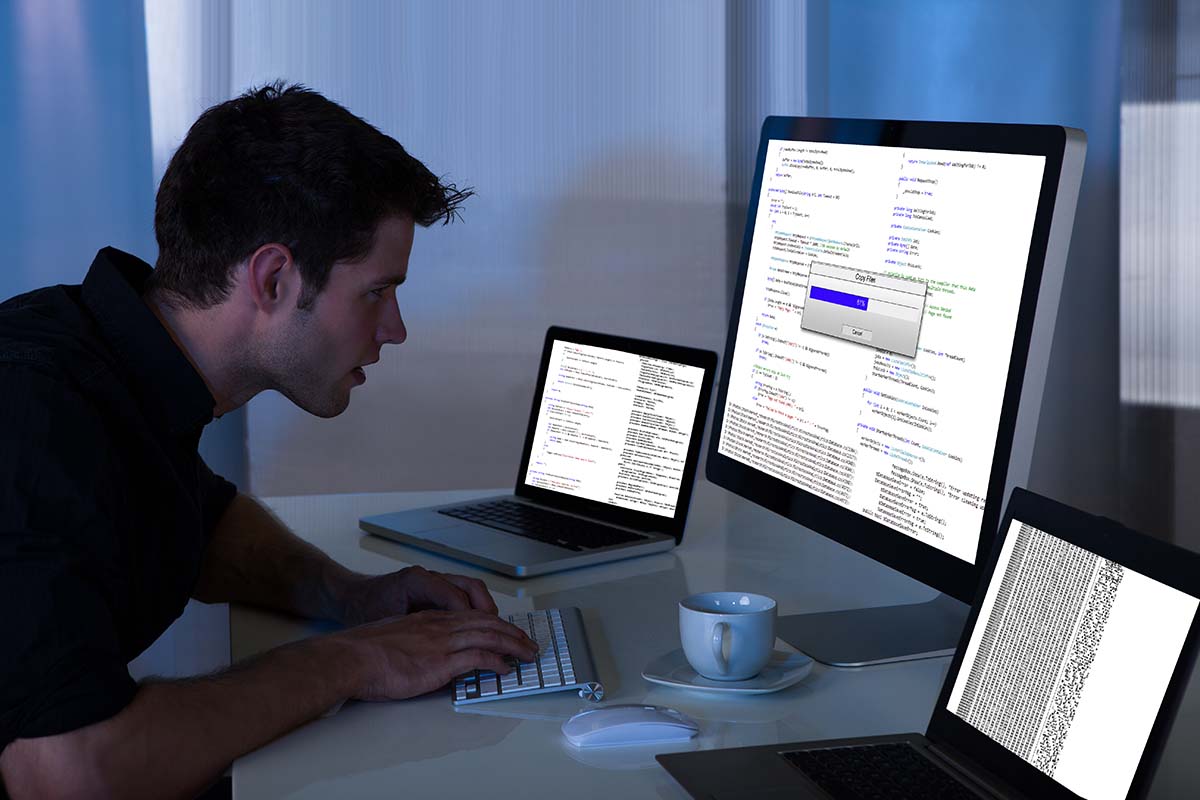 Um homem utiliza três computadores para realizar uma varredura de identificação de fraudes na internet.