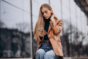 Mulher branca sentada enquanto segura os cabelos com uma mão e outra segura um celular, trazendo o contexto do modelo de Zero Trust aplicado às empresas, em que funcionários estão expostos a riscos de segurança e precisam de monitoramento contínuo.