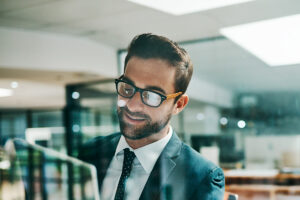 Homem branco de barca e óculos segura um notebook nas mãos enquanto sorri para a tela do aparelho, trazendo o contexto do sucesso de um plano de vendas bem elaborado.