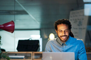 Homem pardo sorrindo enquanto olha para o notebook, provavelmente pesquisando sobre isca digital, tema do artigo.