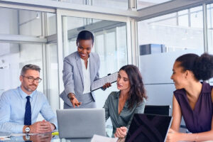 Um homem e três mulheres estão à mesa do escritório discutindo sobre script para prospecção de clientes.