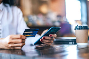 Imagem com uma mulher segurando um cartão de crédito e um celular para representar uma venda segura com o sistema antifraude