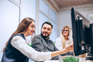 Duas mulheres e um homem sorriem enquanto uma delas aponta para o monitor. Foto ilustra este artigo, sobre Know Your Customer Software.
