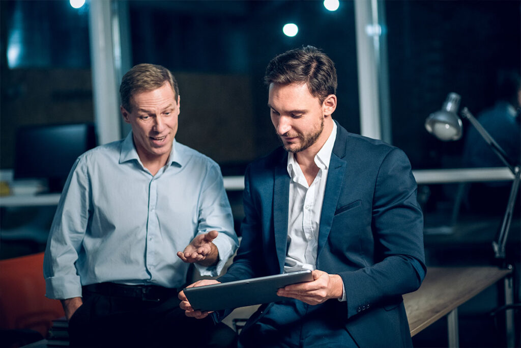 Dois homens brancos conversam enquanto observam a tela de um tablet.