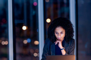 Mulher negra observa a tela do notebook com olhar pensativo, provavelmente refletindo se vale a pena comprar leads segmentados.