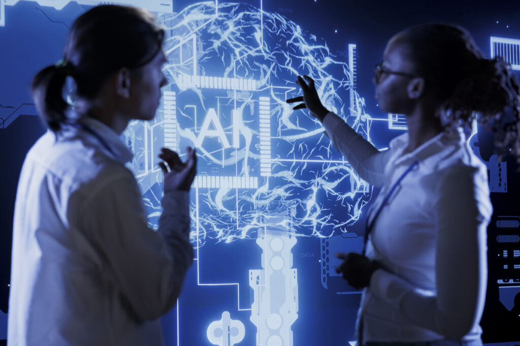 Um homem e uma mulher conversam enquanto apontam para um telão com imagens que representam tecnologia, possivelmente no contexto de como calcular o potencial de mercado com inteligência artificial preditiva.