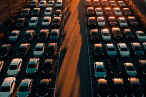 Vários automóveis estacionados e enfileirados em um pátio ao entardecer, trazendo a ideia de frota de veículos no universo do mercado automotivo.