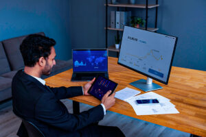 Homem analisa indicadores financeiros em um tablet, com o objetivo de identificar clientes com propensão a investir.