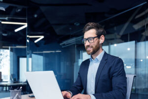 Homem branco digita no teclado do notebook enquanto pesquisa sobre previsibilidade de receita para a empresa em que trabalha.