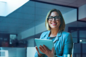 Mulher branca sorrindo enquanto segura um tablet e pesquisa sobre a maturidade financeira da base de clientes de investimentos.