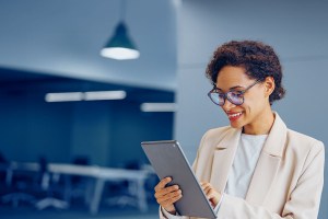 Mulher negra de óculos pesquisa sobre open capital markets em seu tablet enquanto sorri.