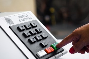 Mão digitando em uma urna eletrônica, trazendo o contexto de doações eleitorais no contexto do compliance empresarial.