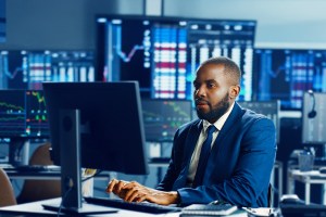 Homem negro digita no teclado do computador corporativo, trazendo o contexto do mercado de capitais e compliance aplicados ao objetivo de como evitar o uso de informações privilegiadas nas instituições financeiras.