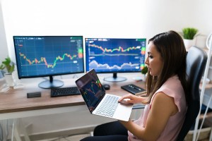 Mulher segura um notebook em uma mão enquanto digita no teclado com a outra, trazendo o contexto de automação de dados no mercado de capitais.