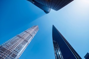 Três prédios altos espelhados com um céu bem azul e ensolarado, trazendo o contexto de empresa de fachada.