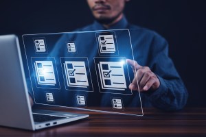Homem branco sentado digita no notebook enquanto uma tela holográfica com quadros de checagem de informação está ao lado da tela, trazendo o contexto de automação de cadastro.