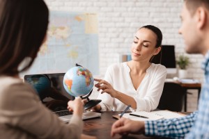 Três pessoas sentadas enquanto uma mulher aponta para o globo em cima de uma mesa, trazendo o contexto de como acompanhar o fluxo estrangeiro na bolsa de valores.