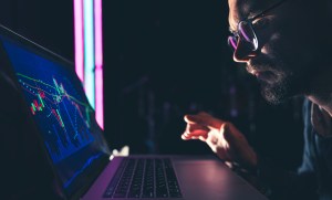 Um homem analisando gráficos do mercado de ações e dados financeiros em um quadro eletrônico, trazendo o contexto de casos de insider trading no Brasil​ e no mundo.