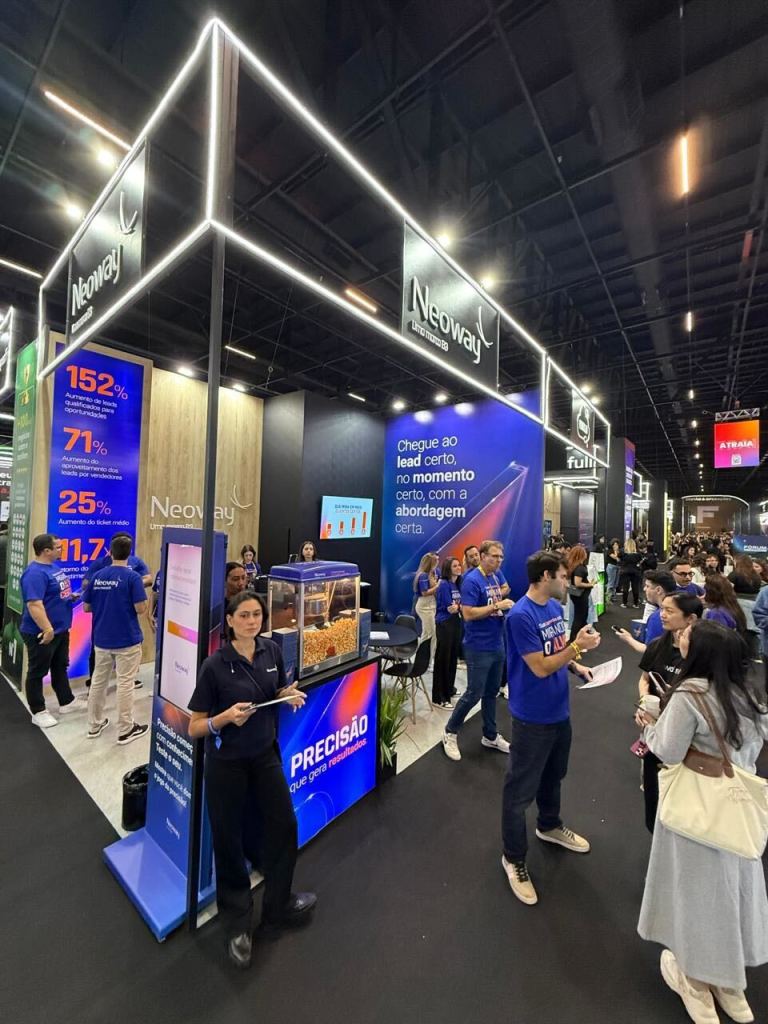 Estande da Neoway no Fórum E-commerce Brasil 2025 com funcionários e participantes do evento.